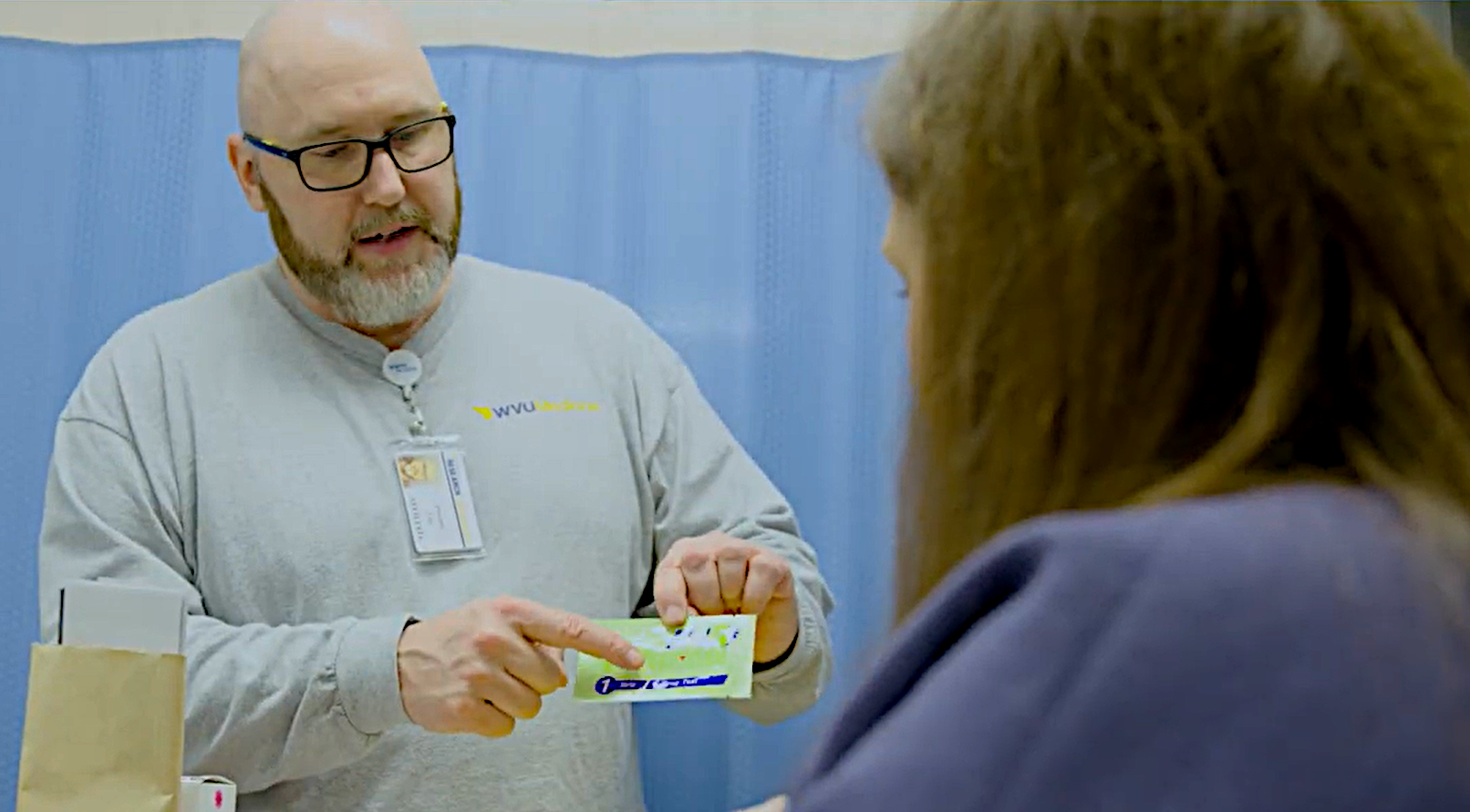 A peer presenting free naloxone medication with instructions to a patient that is visiting the ER.