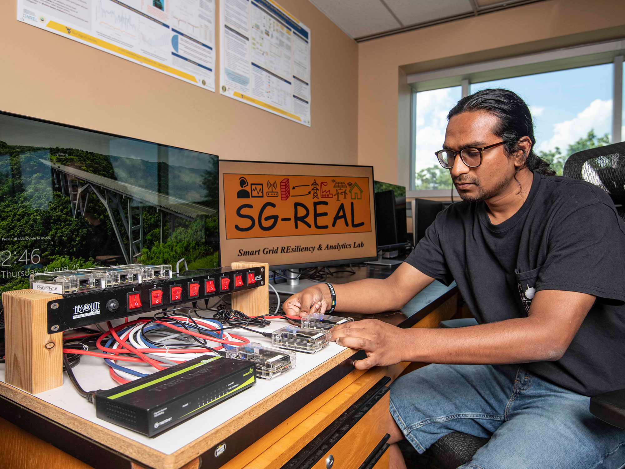 A research seated at a workstation with the SG Real project.  There are two computer monitors with electronics wired together on the desk.